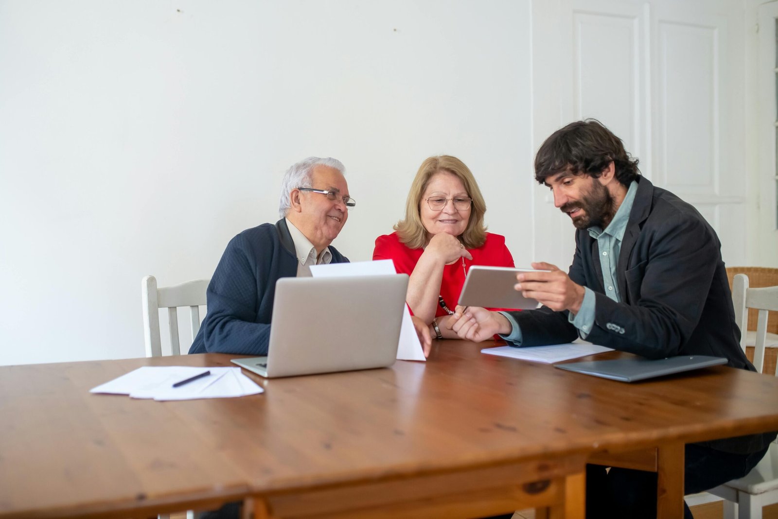 Two senior clients and a consultant discussing documents and using a tablet in a modern office.